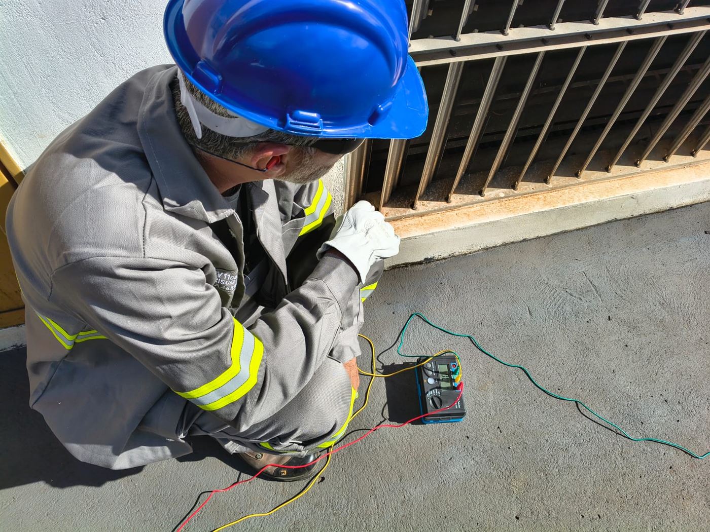 Profissional com EPI completo executando ensaio de resistência de aterramento junto à edificação