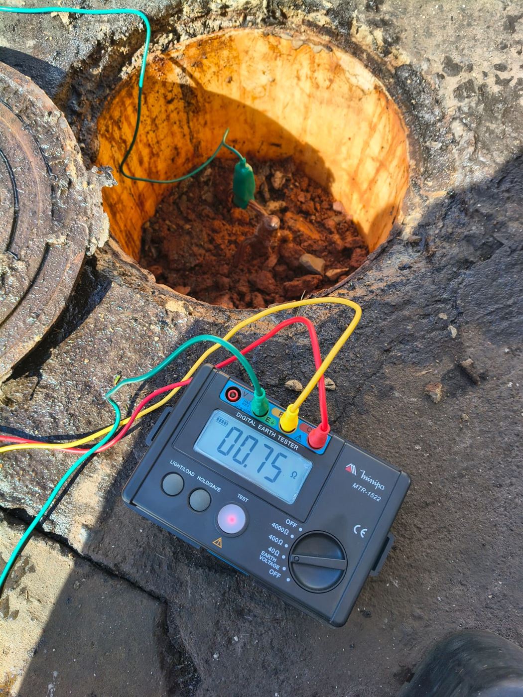 Terrômetro digital em caixa de inspeção de aterramento indicando 0,75 ohm durante medição
